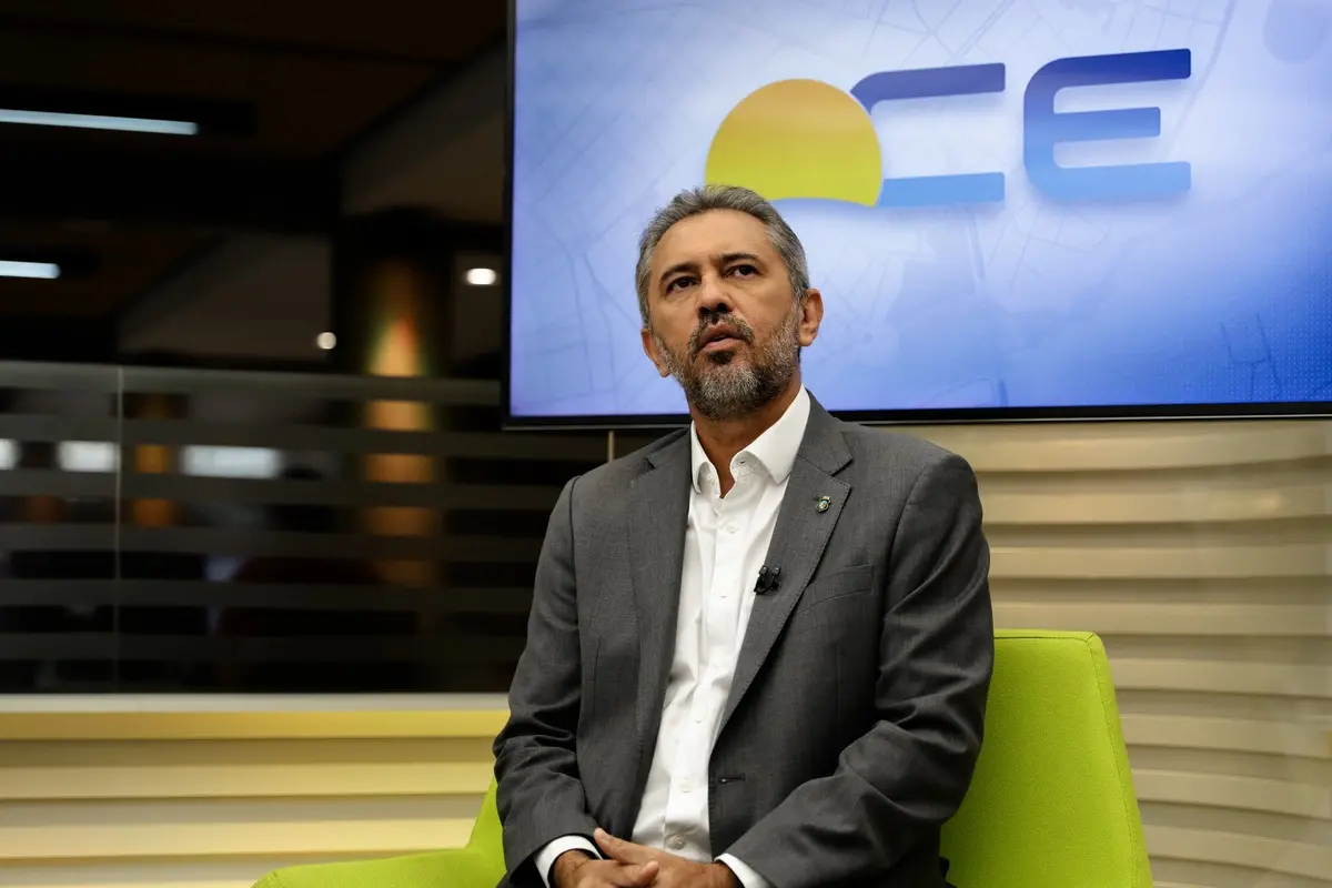 Elmano usa terno azul marinho e caminha branca. Está sentado no estúdio do CETV, gesticulando durante entrevista