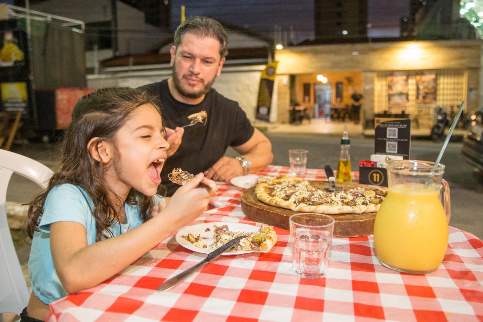 Na imagem, pai e filha consomem pizza da pizzaria Pizza da Praça, localizada no bairro de Fátima