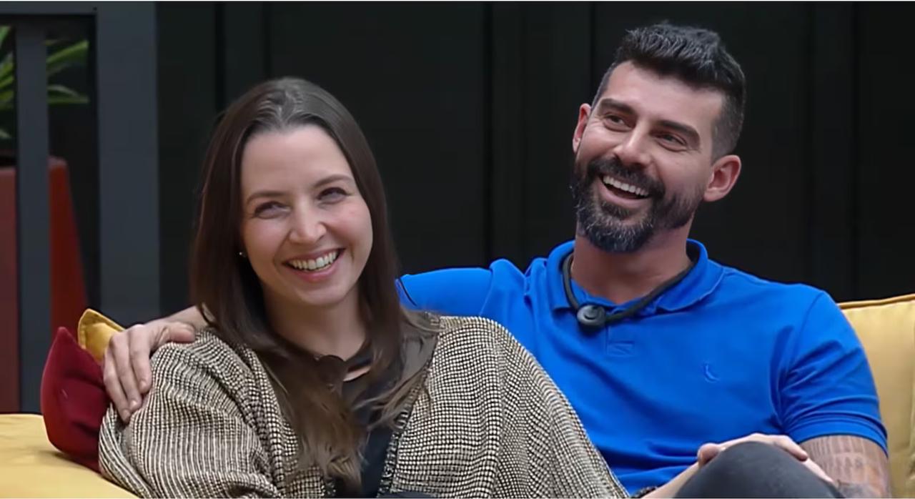 Carol e Radamés, casal de participantes do reality show Power Couple, sorrindo abraçados e sentados, ilustram resultado do casal vencedor do programa