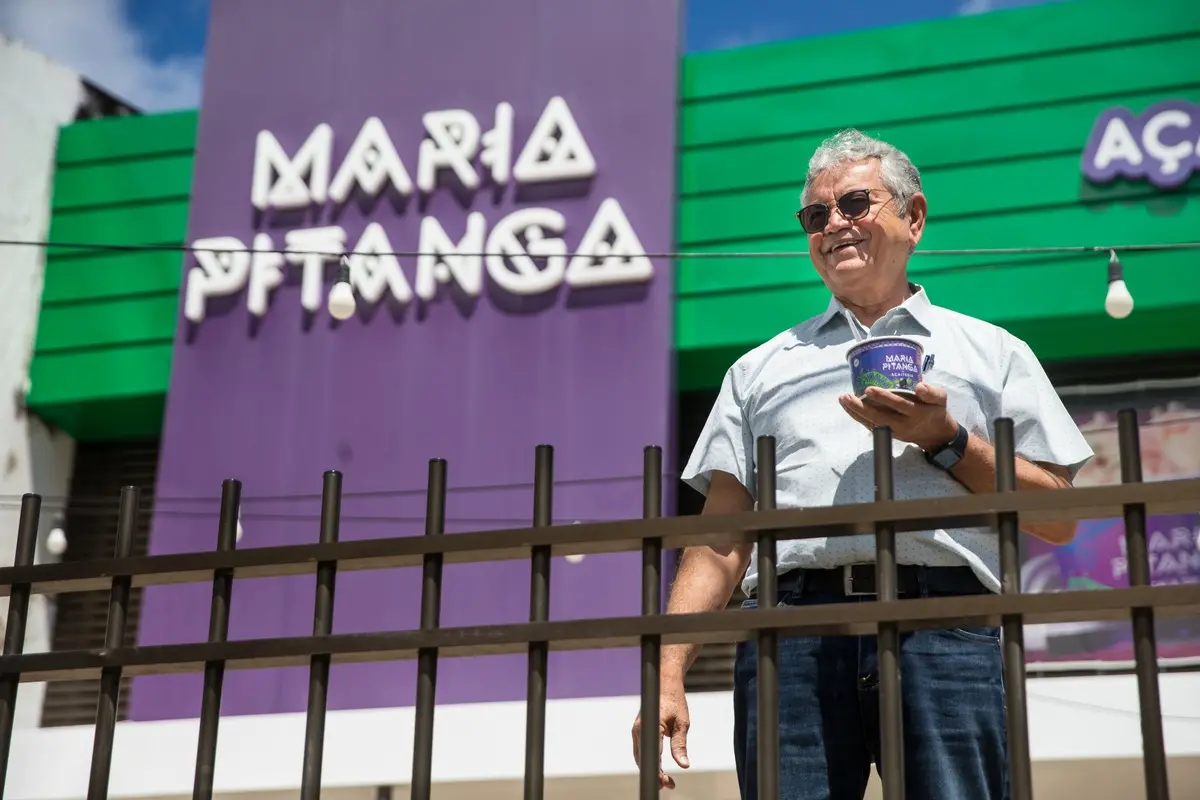 Homem grisalho em frente à loja que tem fachada Maria Pitanga