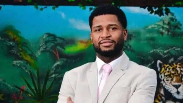 Foto de um homem negro posando para foto. Guilherme usa terno creme e gravata rosaa