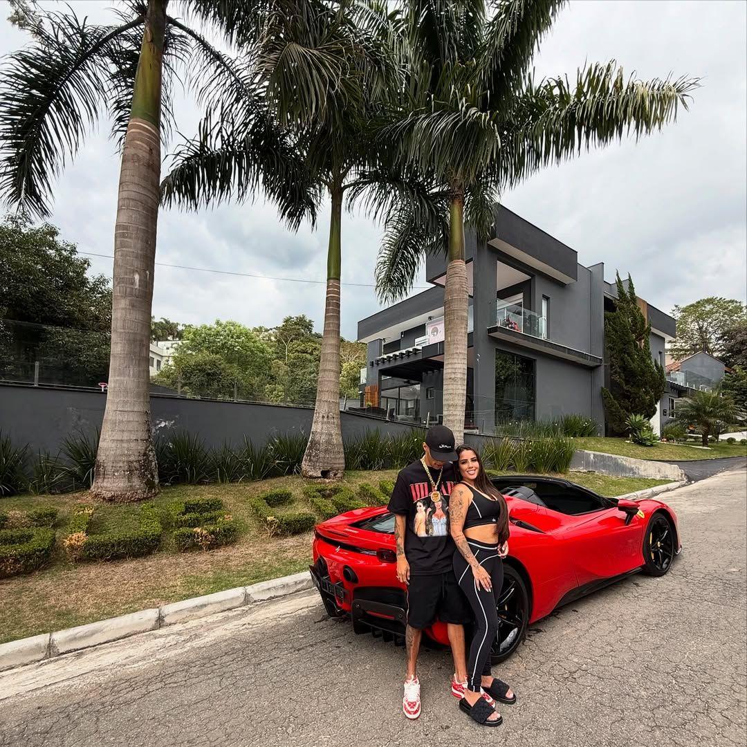 buzeira ao lado de esposa, diante de carro de luxo vermelho e mansão