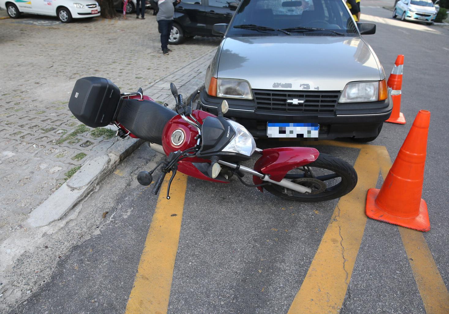 Imagem mostra moto vermelha deitada sobre o asfalto, na frente de um carro cinza que colidiu com ela