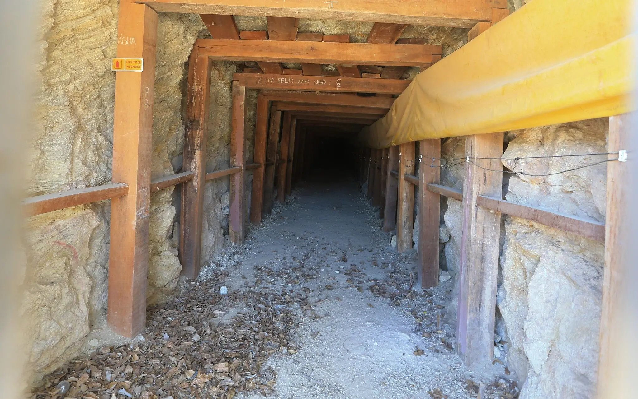 Foto de galeria subterrânea em Santa Quitéria com estrutura de madeira de sustentação, ventilação por lona amarela e folhas secas no chão.