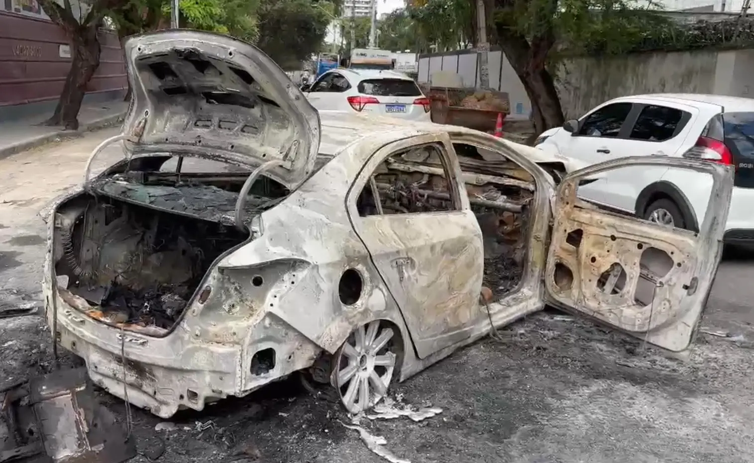 Foto de carro Prisma após incêndio, cheio de fuligem, sem pneus e com cobertura branca