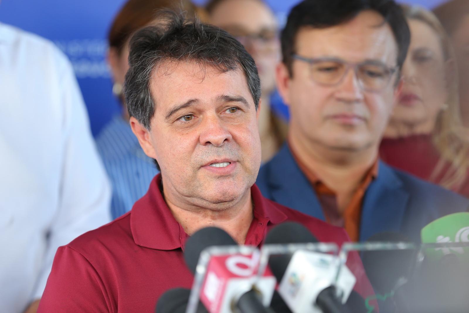 Imagem mostra o prefeito de Fortaleza, Evandro Leitão, discursando à imprensa diante de microfones em evento sobre o ITA Ceará, em Fortaleza. Ele veste uma camisa de gola polo cor de vinho. Atrás dele, embaçado em segundo plano, aparece o reitor da UFC, Custódio Almeida.