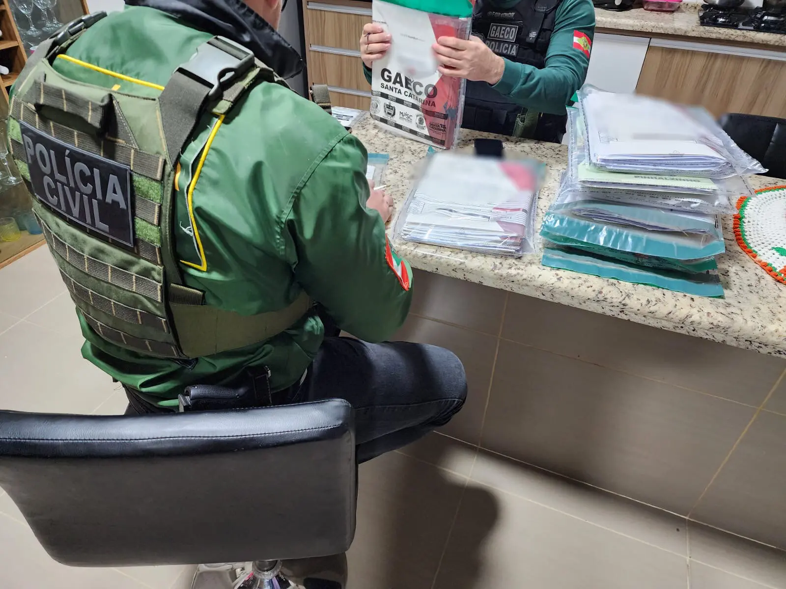 Fogo de cumprimento de mandado durante a Operação Entre Lobos, divulgada pelo Ministério Público de Santa Catarina. Policias analisam documentos em uma residência