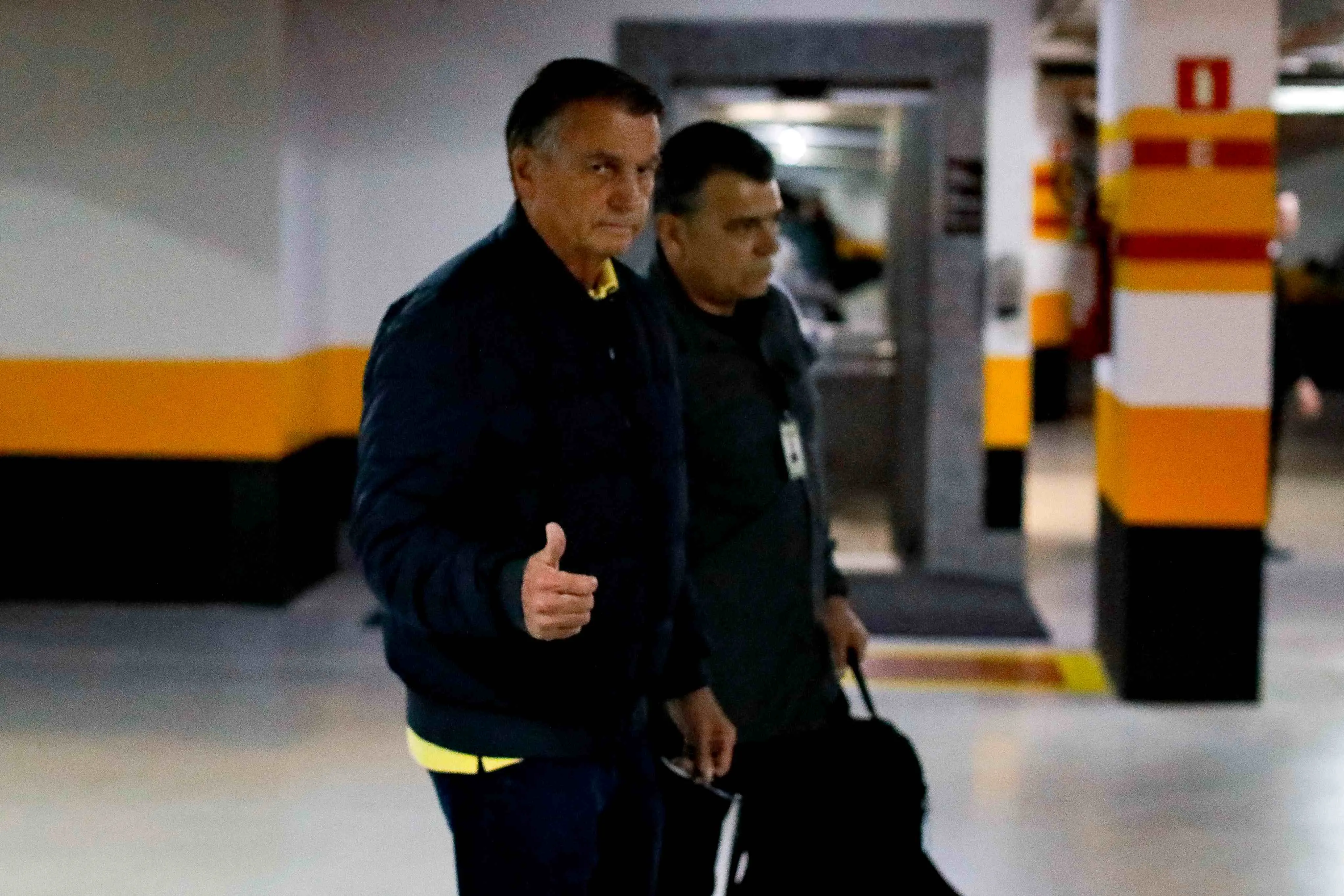 Imagem do ex-presidente brasileiro Jair Bolsonaro (E) fazndo sinal de positivo ao deixar a sede do Partido Liberal em Brasília, em 22 de julho