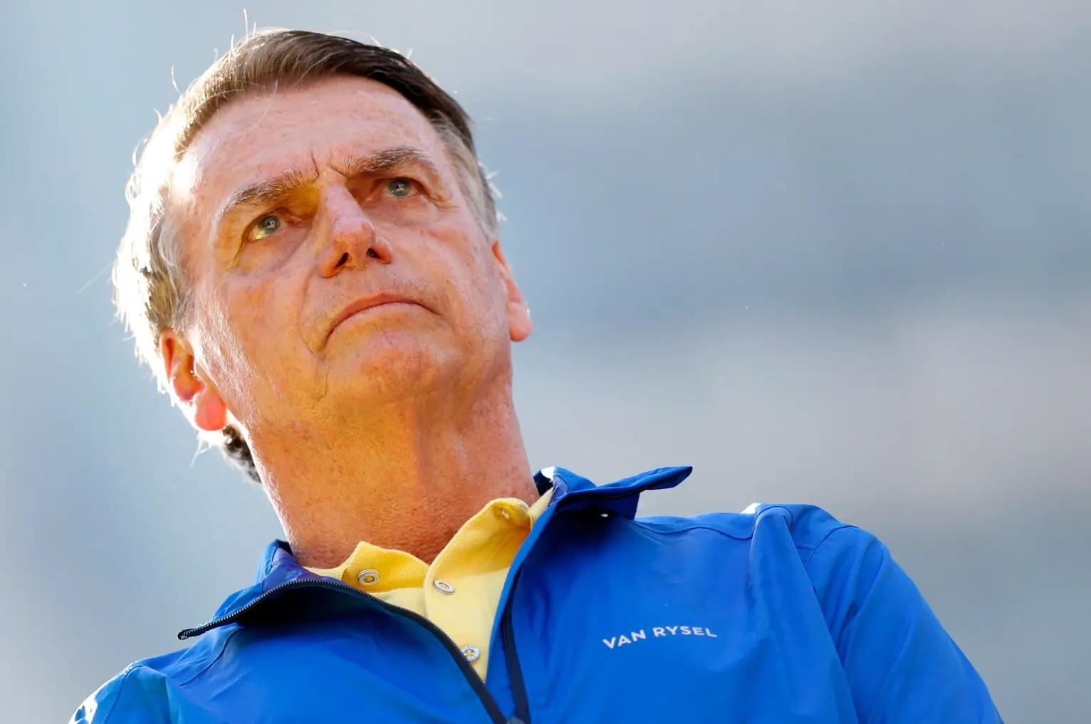 Jair Bolsonaro com semblante sério. Ele está com casaco azul e blusa gola polo amarela