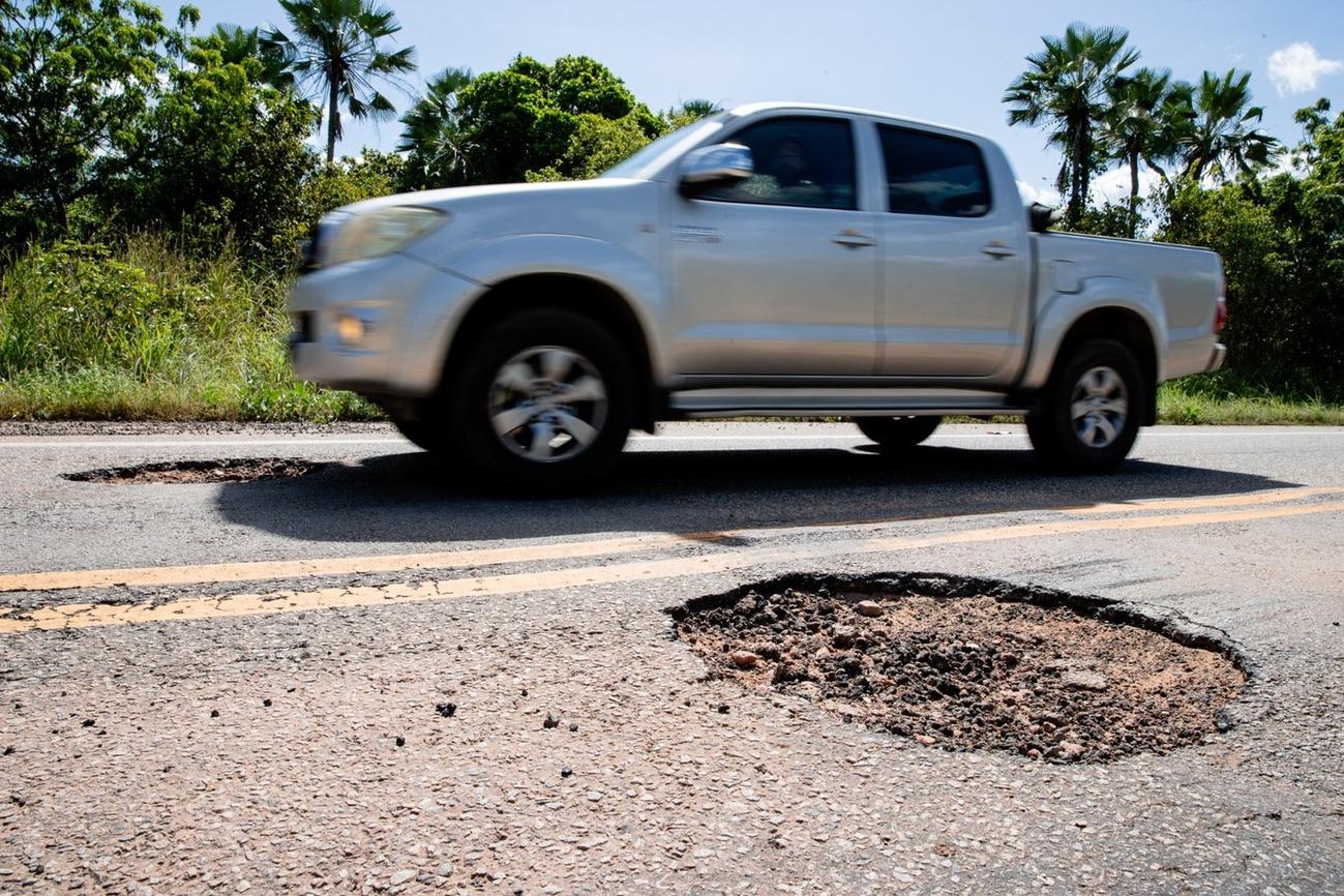 Foto que contém carro trafegando pela CE-156 com buracos no asfalto