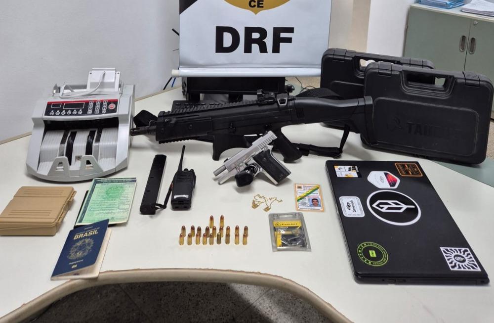 Foto de um material apreendido com dois suspeitos de cometer um furto milionário em Fortaleza. Em cima de uma mesa, há duas armas de fogo, munições, documentos e uma máquina de contar dinheiro