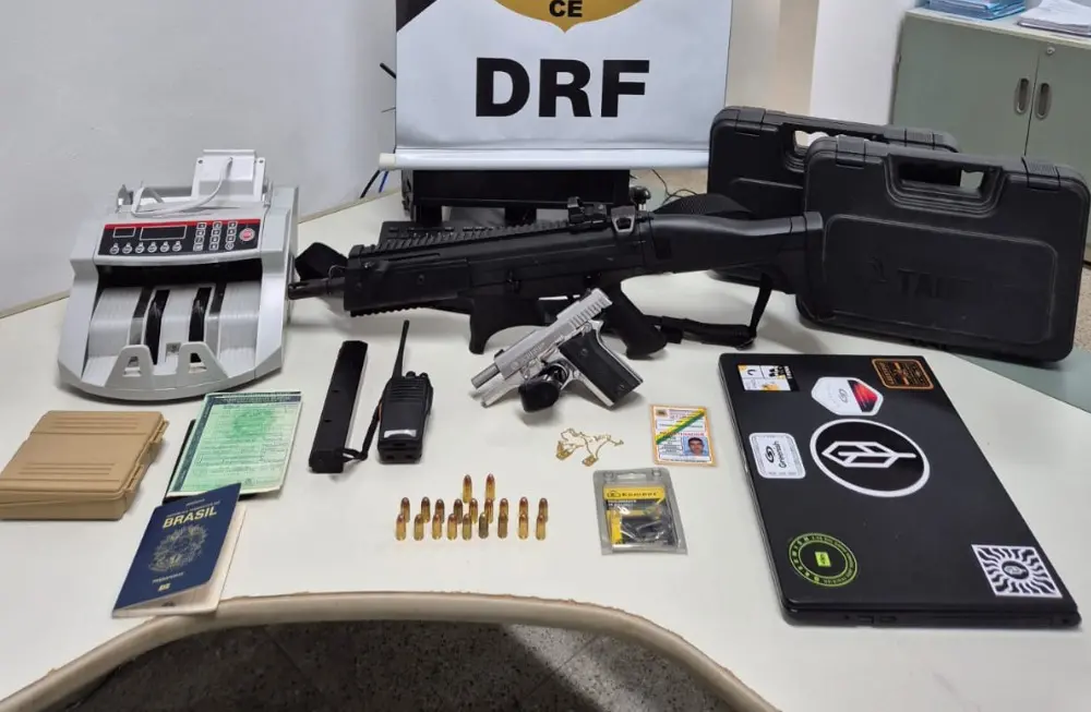 Foto de um material apreendido com dois suspeitos de cometer um furto milionário em Fortaleza. Em cima de uma mesa, há duas armas de fogo, munições, documentos e uma máquina de contar dinheiro