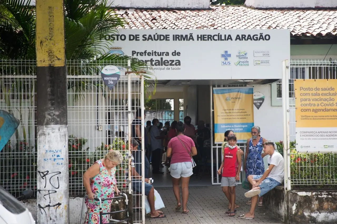 Imagem mostra entrada do posto de saúde Irmã Hercília Aragão, em Fortaleza, com diversos pacientes na frente, aguardando atendimento.