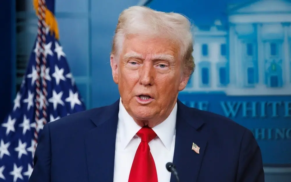 Donald Trump é um homem idoso de cabelos e sobrancelhas brancas e na foto está de terno azul, camisa social branca e gravata vermelha