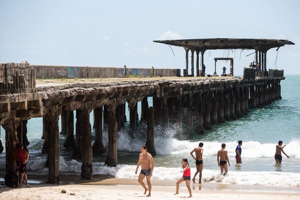 imagem de uma ponte em ruínas sobre o mar de Fortaleza e banhistas nas proximidades da ponte