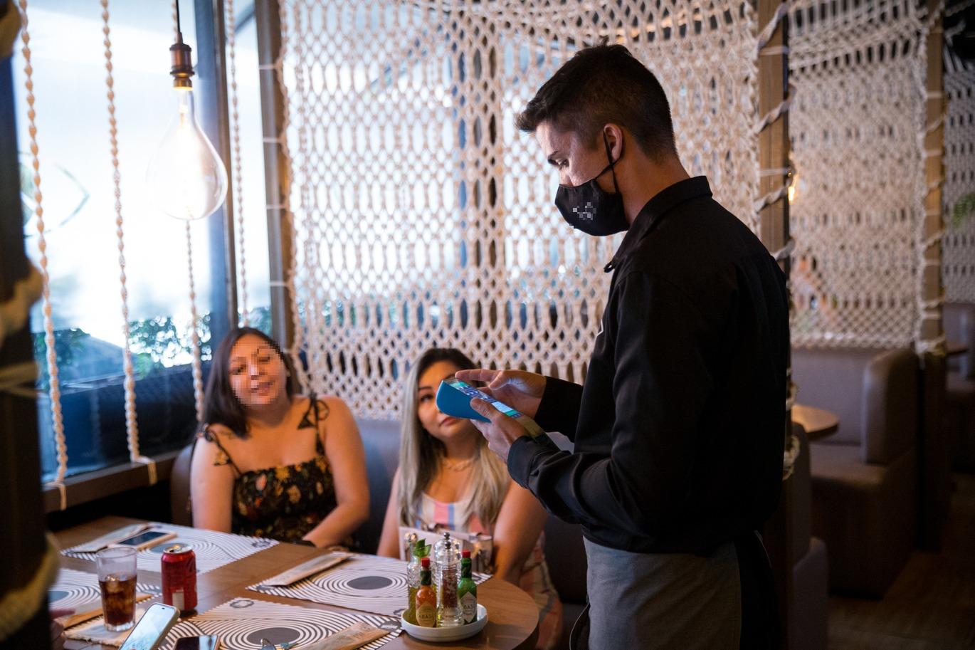 Foto que contém garçom recebendo pagamento em restaurante de Fortaleza