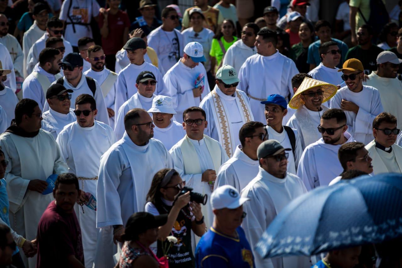 Multidão de pessoas reunidas ao ar livre, muitas vestindo roupas brancas, em um evento religioso ou celebração com clima ensolarado.