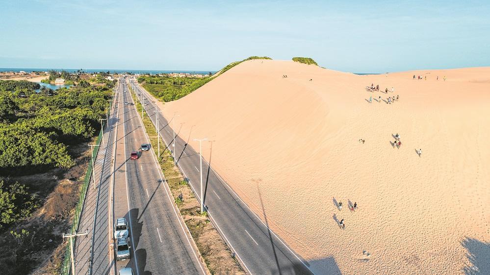 Imagem aérea mostra duna da Sabiaguaba, em Fortaleza. No meio da foto, a avenida duplicada separa as dunas da vegetação.