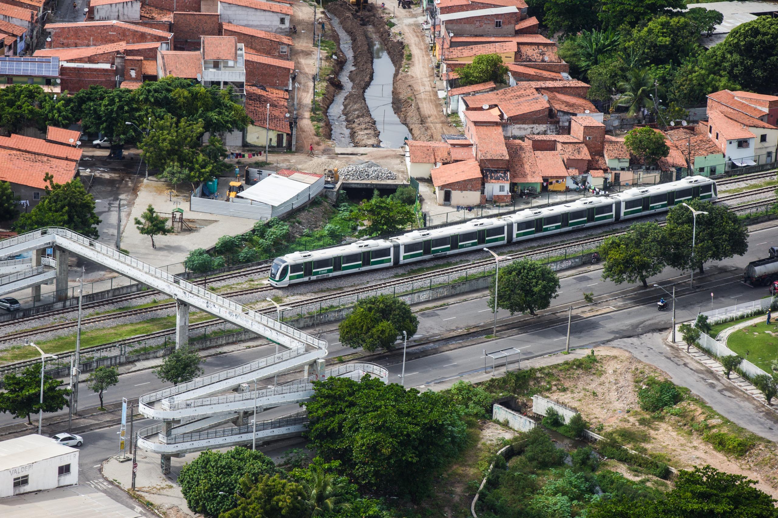 Imagem aérea mostra metrô chegando a uma estação. Ao redor, casas e prédios de Fortaleza.