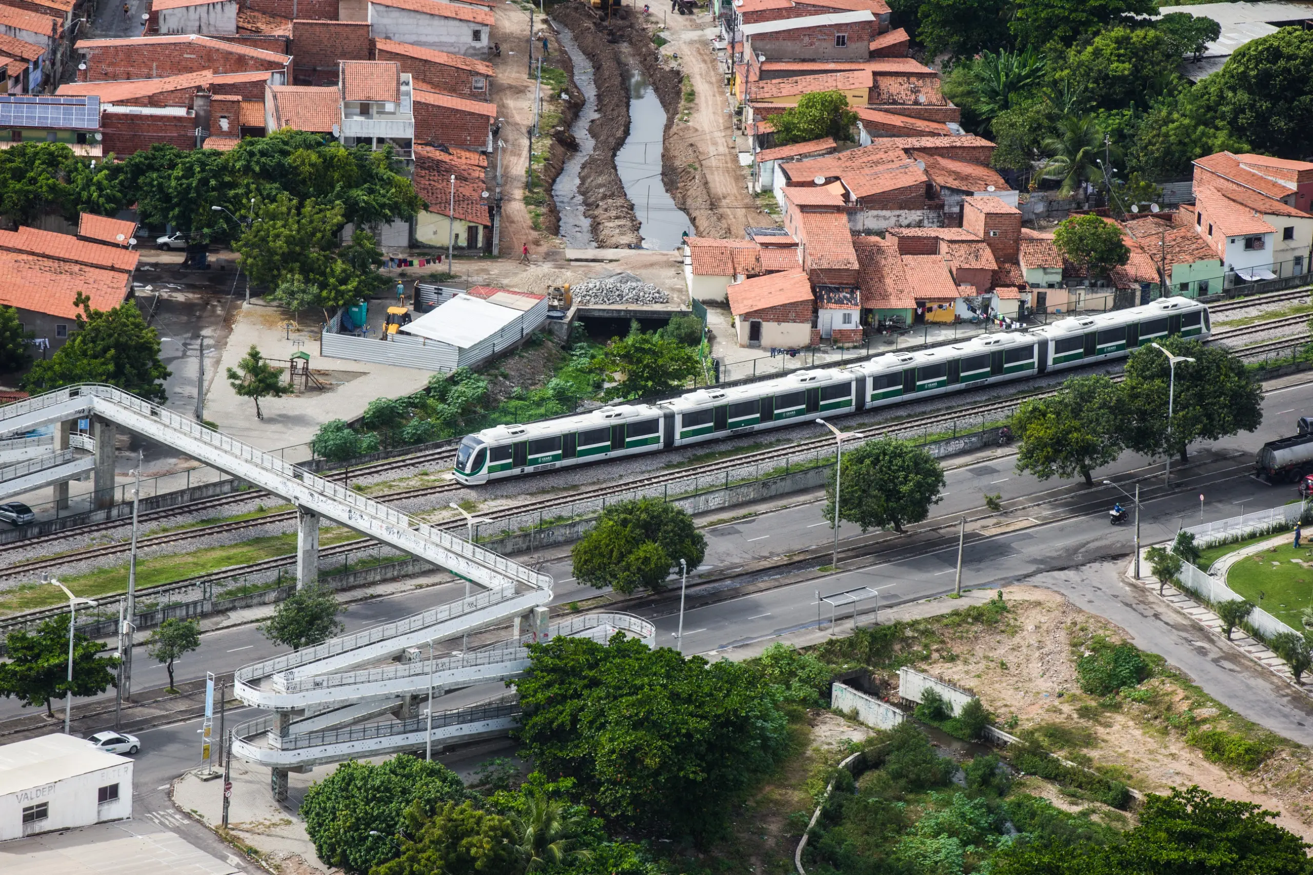 Imagem aérea mostra metrô chegando a uma estação. Ao redor, casas e prédios de Fortaleza.