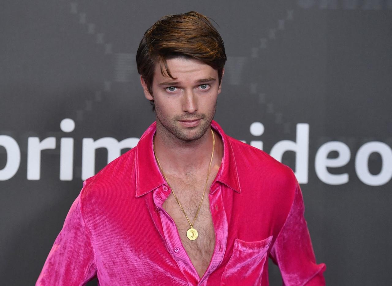 Ator Patrick Schwarzenegger de roupa rosa em frente a um painel preto no desfile da Fenty