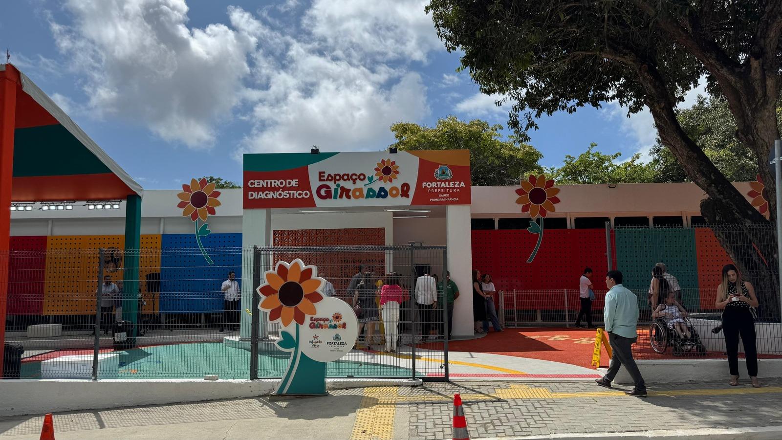 Imagem mostra fachada do Centro de Diagnóstico Espaço Girassol, para atendimento de crianças e adolescentes com suspeita de autismo e outros transtornos do desenvolvimento em Fortaleza. O prédio tem desenhos de girassóis e detalhes muito coloridos. Acima, o céu azul com nuvens brancas. Ao lado, uma árvore frondosa.