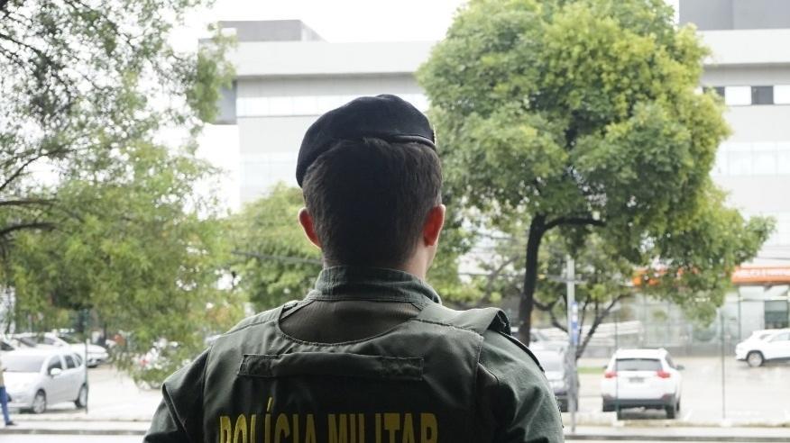 Foto genérica de policial militar, fardado, de frente para prédio da SSPDS em Fortaleza