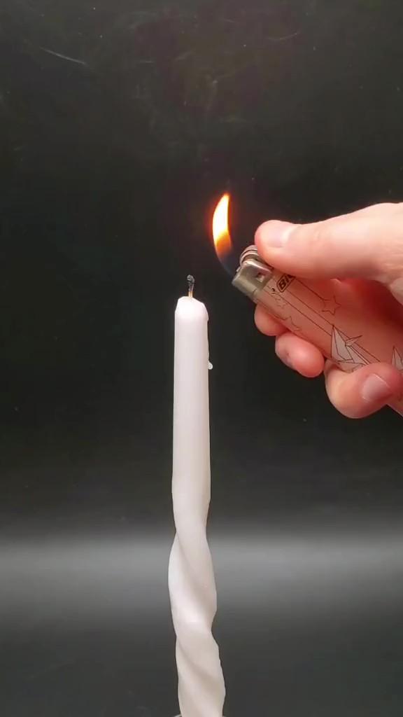 Pessoa acendendo uma vela com isqueiro, demonstrando um experimento de acender vela pela fumaça, em um vídeo registrado por câmera de celular.
