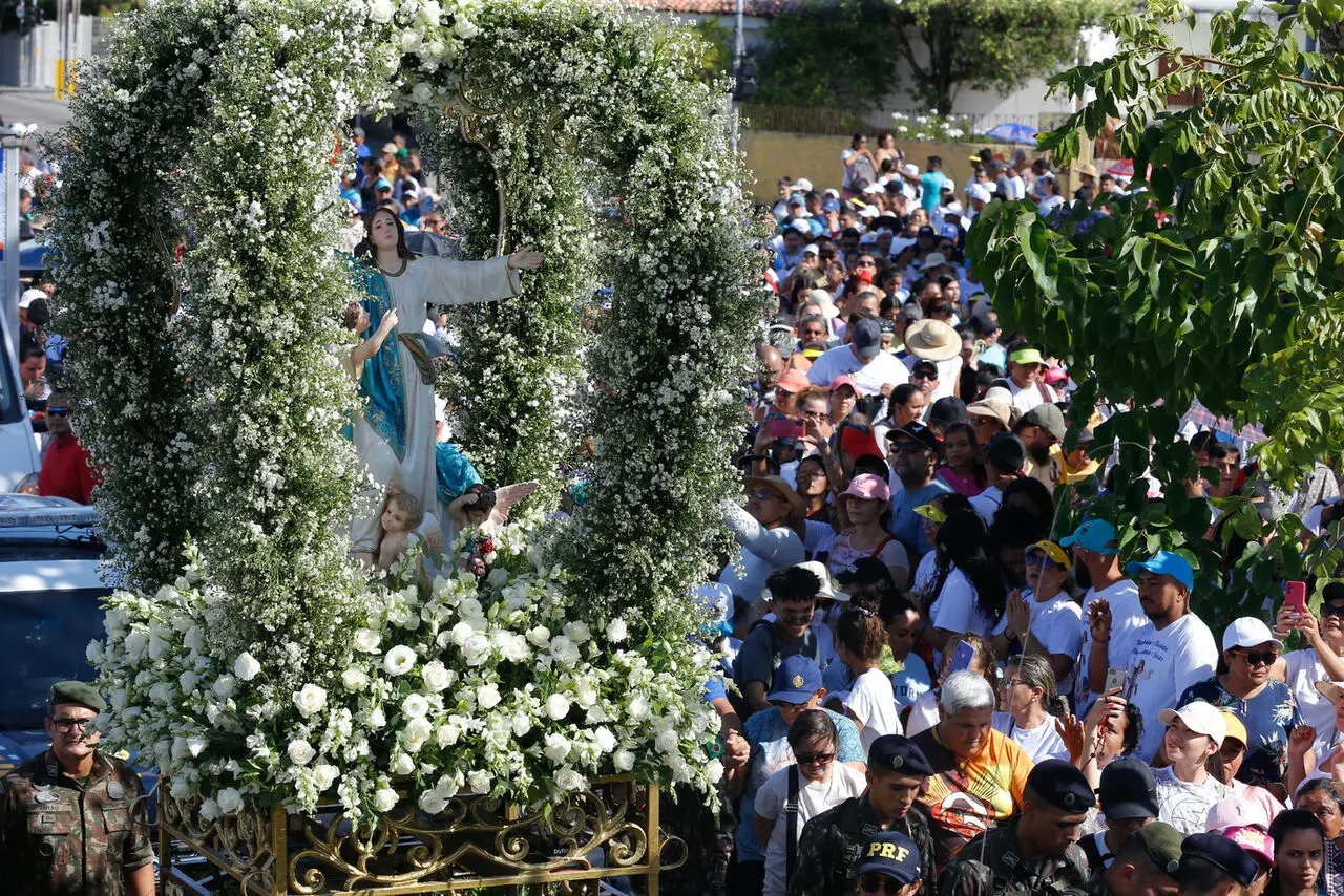 Imagem mostra tradicional procissão Caminha com Maria com grande aglomeração de fiéis celebrando a padroeira de Fortaleza, Nossa Senhora da Assunção, com destaque para a imagem da santa apesentada em uma estrutura decorada com flores brancas, ilustrando se 15 de agosto é feriado em Fortaleza