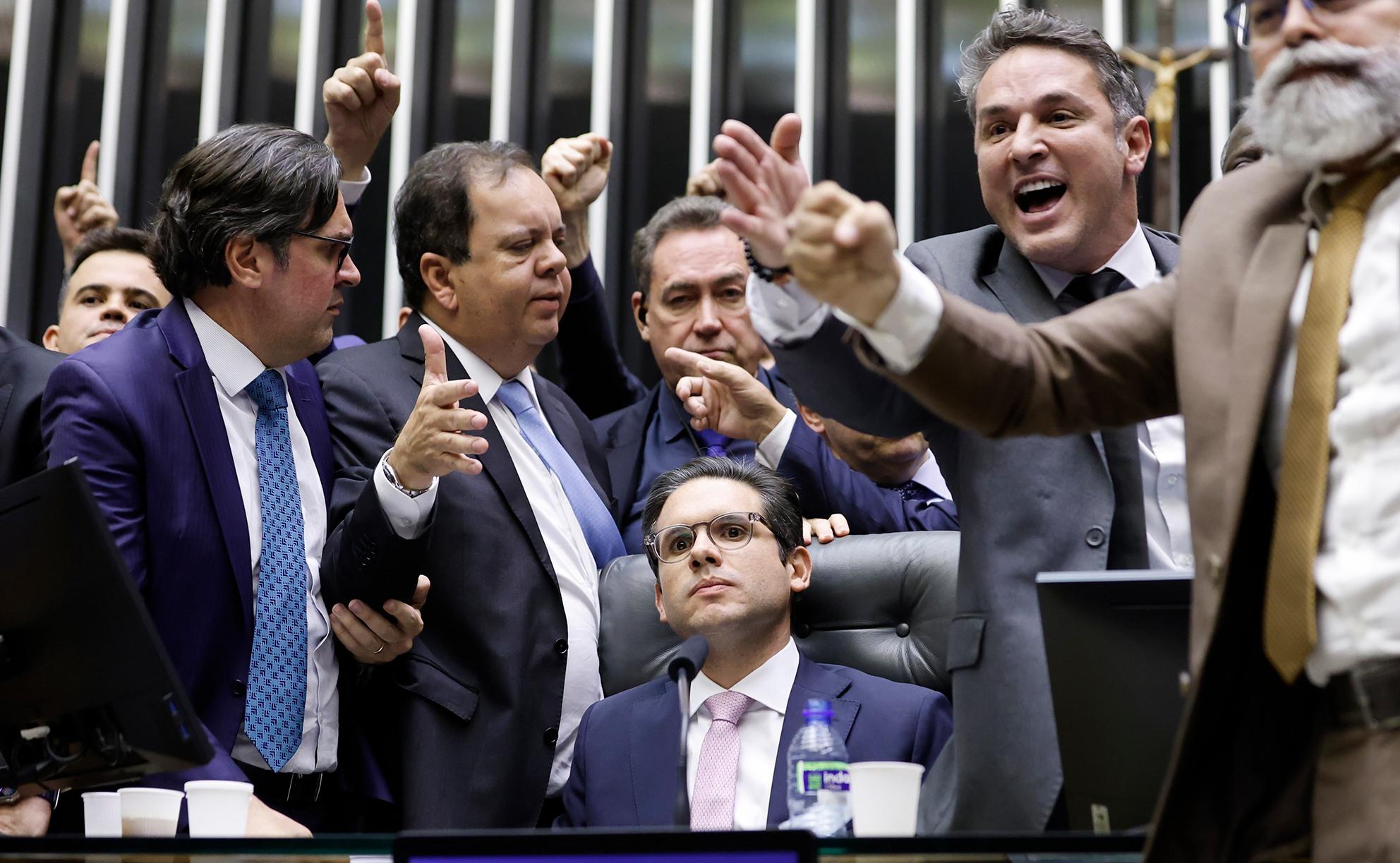 Hugo Motta ao lado de deputados. Ele está sentado no centro da Mesa Diretora e, em seu entorno, estão outros deputados