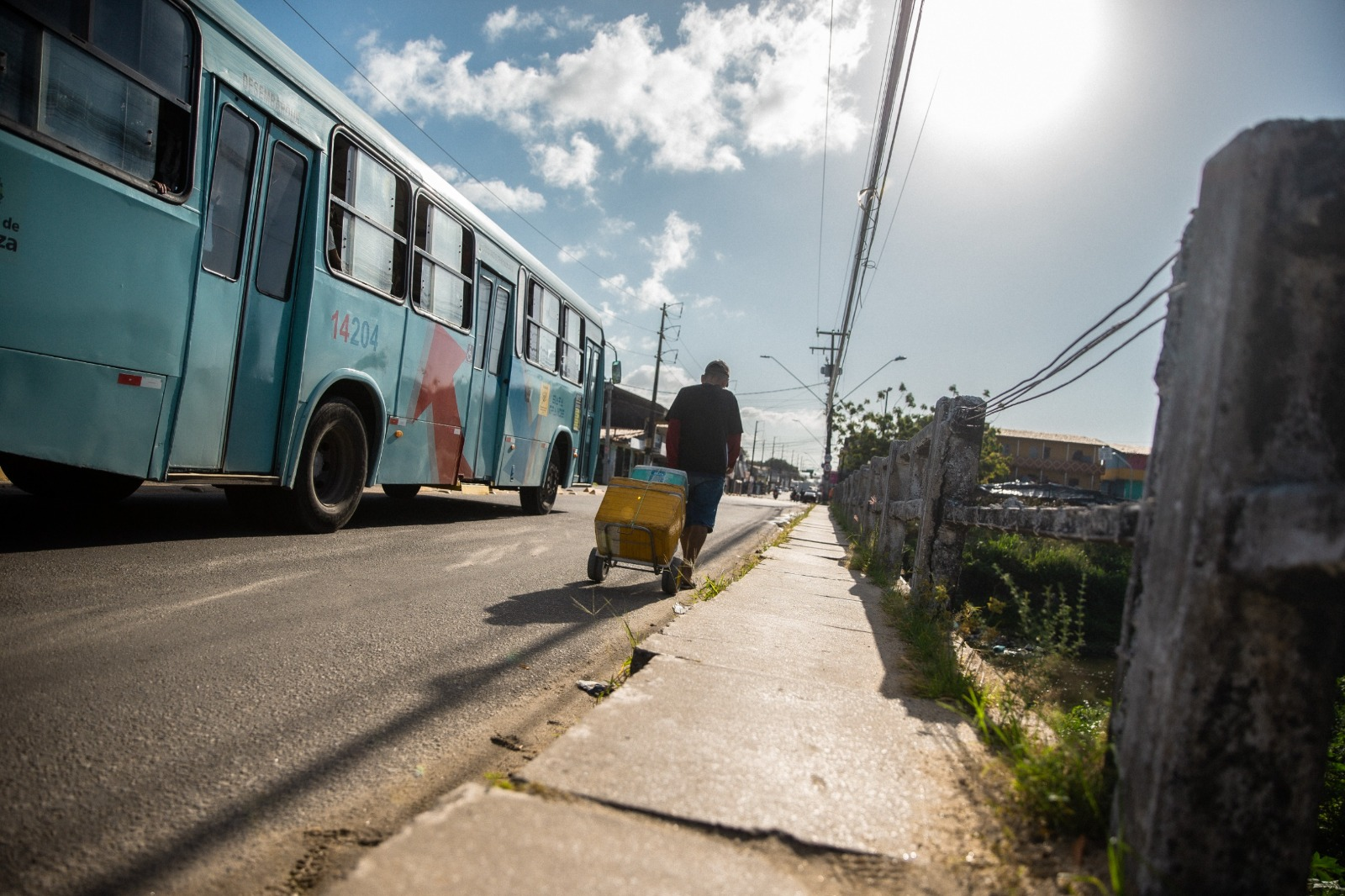 Foto que contém ambulante trafegando por via do bairro Genibaú ao lado de um ônibus