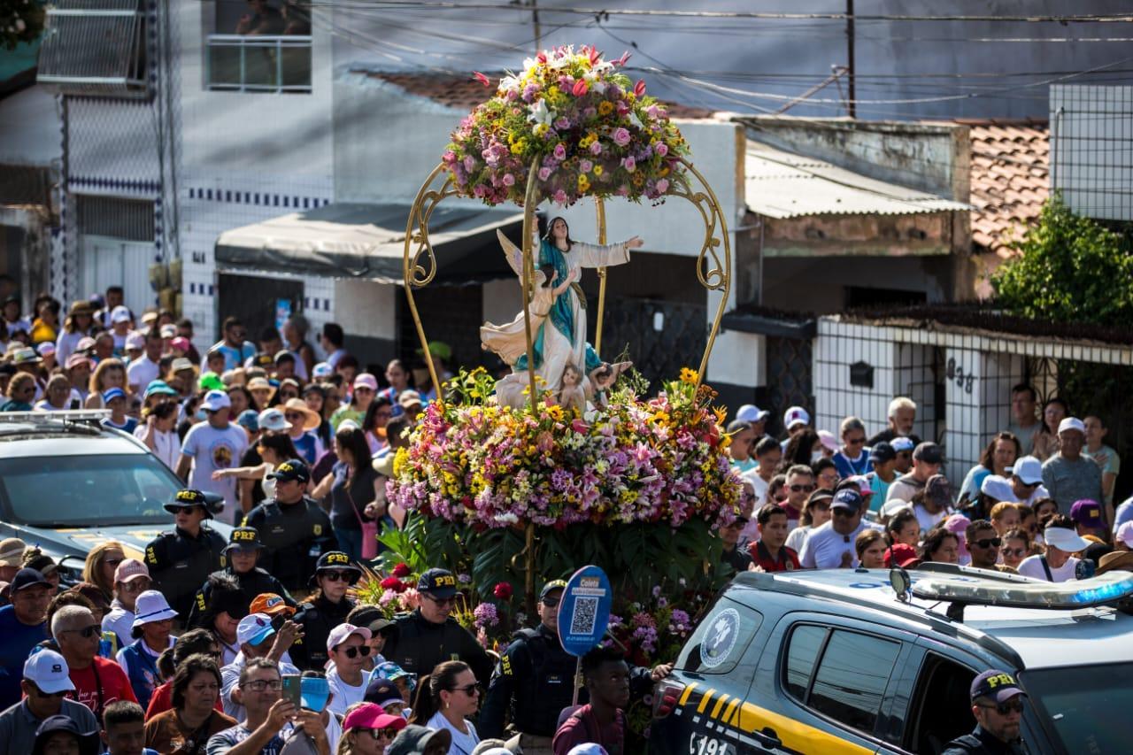 Procissão com imagem de Nossa Senhora da Assunção, rodeada por uma grande multidão de fiéis e pessoas participando de celebração religiosa na rua.