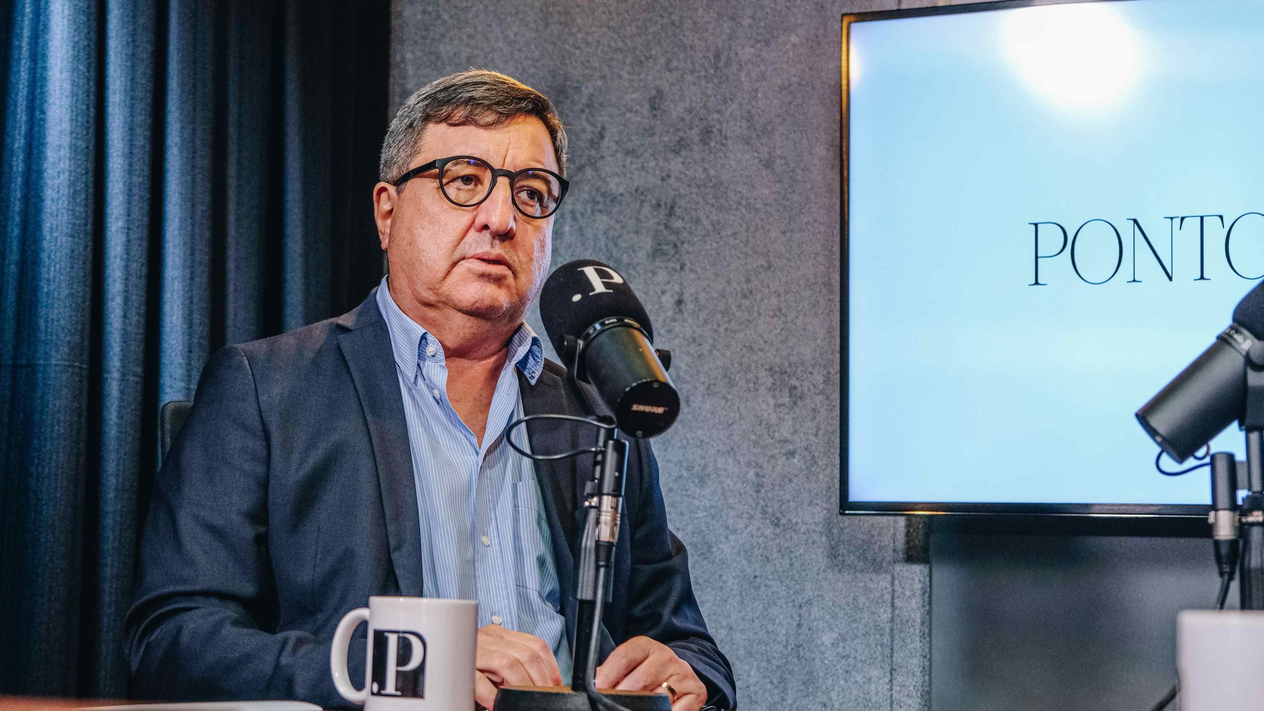 Na imagem, o deputado federal Danilo Forte (União) aparece sentado em um estúdio de gravação, vestindo paletó azul-escuro e camisa social azul-clara, sem gravata. Ele usa óculos de armação escura e mantém uma expressão séria enquanto fala ao microfone, que exibe a letra “P” — símbolo do programa PontoPoder