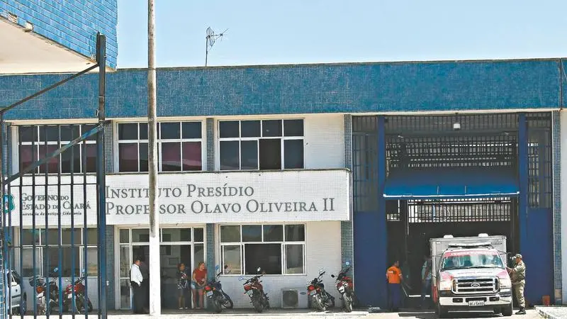Fachada do Instituto Presídio Professor Olavo Oliveira II (IPPOO II), em Fortaleza (CE). Pessoas são vistas na entrada do prédio. Ambulância está posicionada no portão principal da unidade prisional.