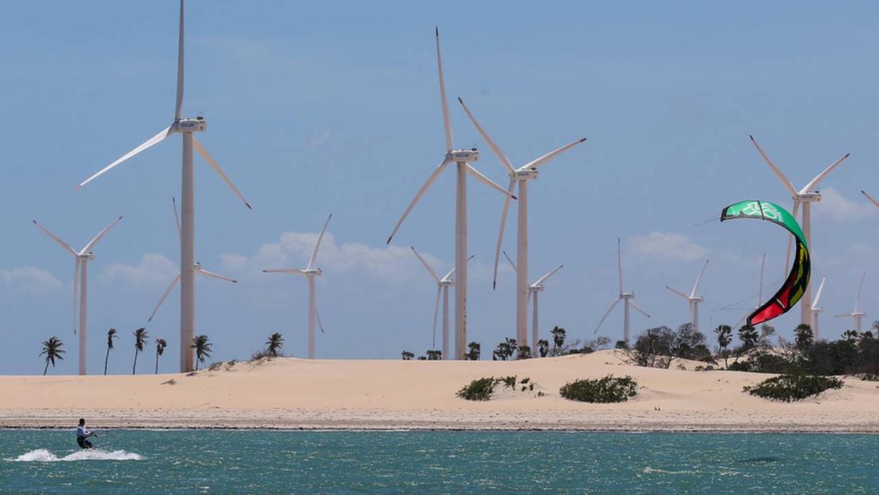 Ao fundo da paisagem do mar, uma faixa de areia com turbinas eólicas