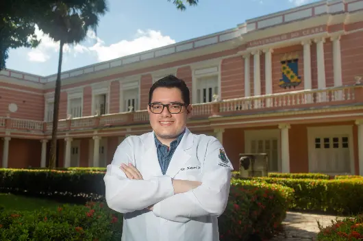 Howard Ribeiro Lopes Junior, homem de cabelo preto vestido com jaleco branco na frente de prédio com características históricas