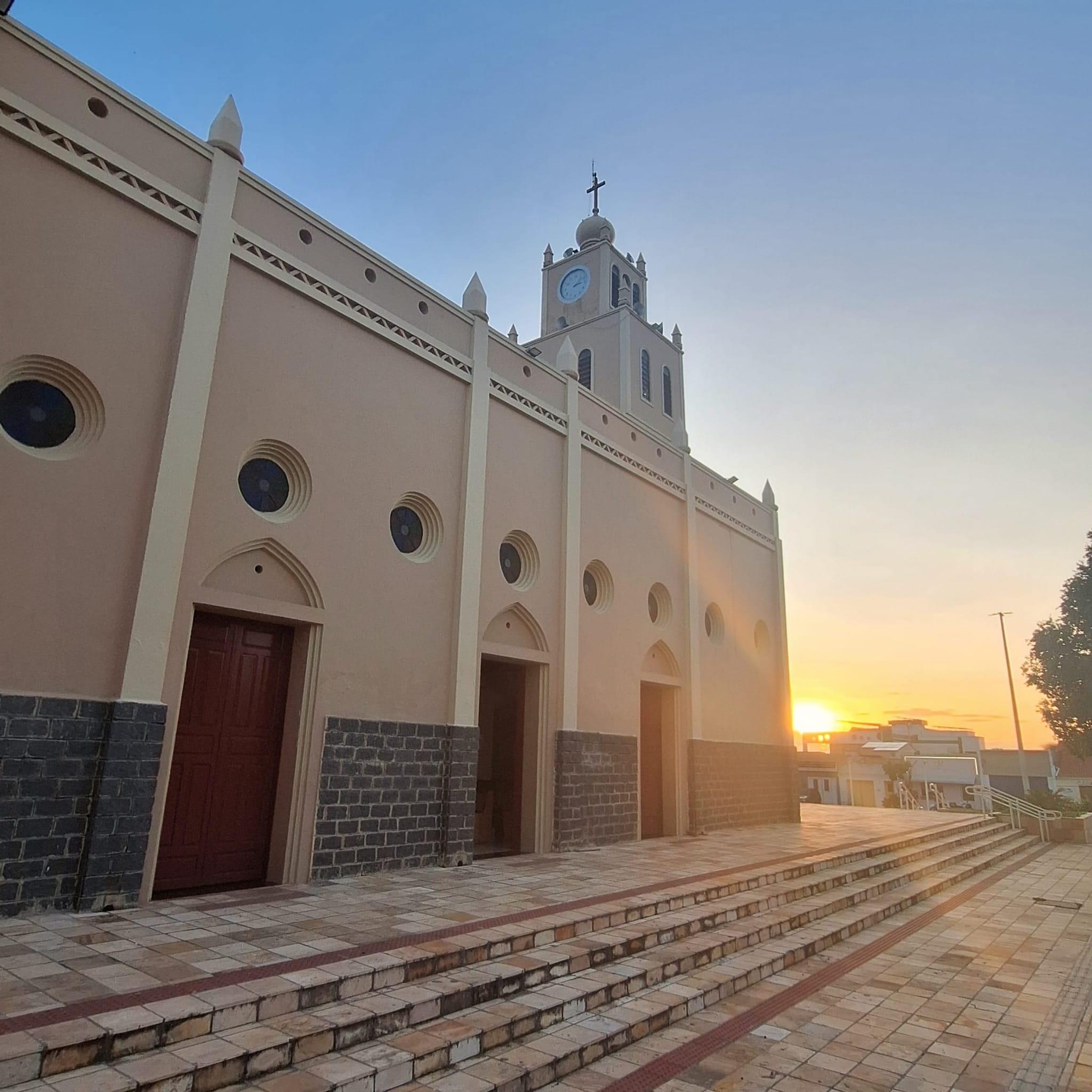 Imagem da lateral do Santuário Diocesano da Divina Misericórdia, Igreja Católica no Município de Barro, no Ceará. As paredes são pintadas de bege e, ao fundo, o sol estende raios solares.