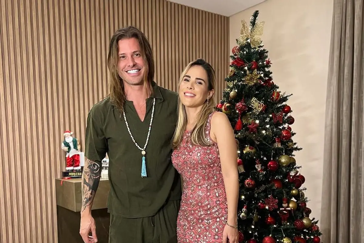 Wanessa Camargo e Dado Dolabella sorrindo ao lado de uma árvore de Natal decorada para o Natal em uma sala com decoração elegante.