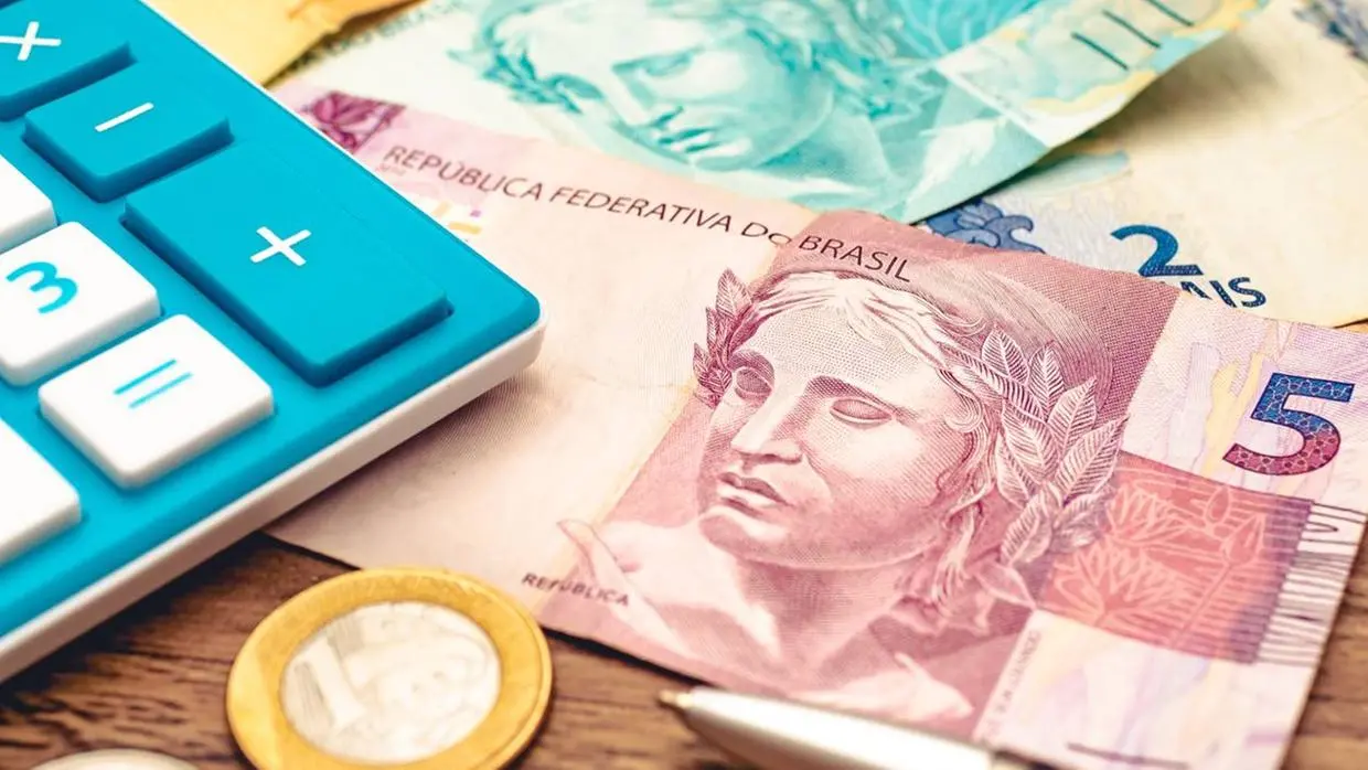 Imagem mostra notas de dinheiro, moedas e uma calculadora