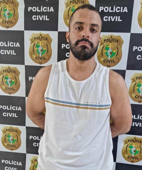 Matheus Anthony com as mãos algemadas na delegacia da Polícia Civil do Ceará. Ele é um homem de meia idade, barba por fazer e que está de camisa branca regata