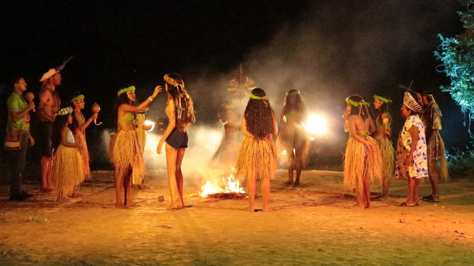 Foto de pessoas Kariri em trajes tradicionais indígenas dançam em círculo ao redor de uma fogueira durante a noite, em Crateús
