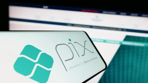 Imagem mostra tela de celular e tela de computador ao fundo com a logo do Pix, sistema de pagamentos do Banco Central