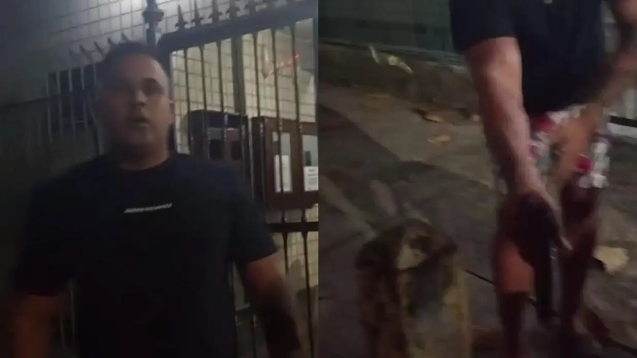 Imagem dividida em duas partes. À esquerda, um homem de camiseta preta está de frente para a câmera, em frente a um portão de grade metálica, com expressão séria. À direita, vê-se parte inferior do corpo do mesmo homem com bermuda estampada, segurando uma arma de fogo apontada para baixo. O chão está sujo com o que parece ser sangue e há folhas secas espalhadas.