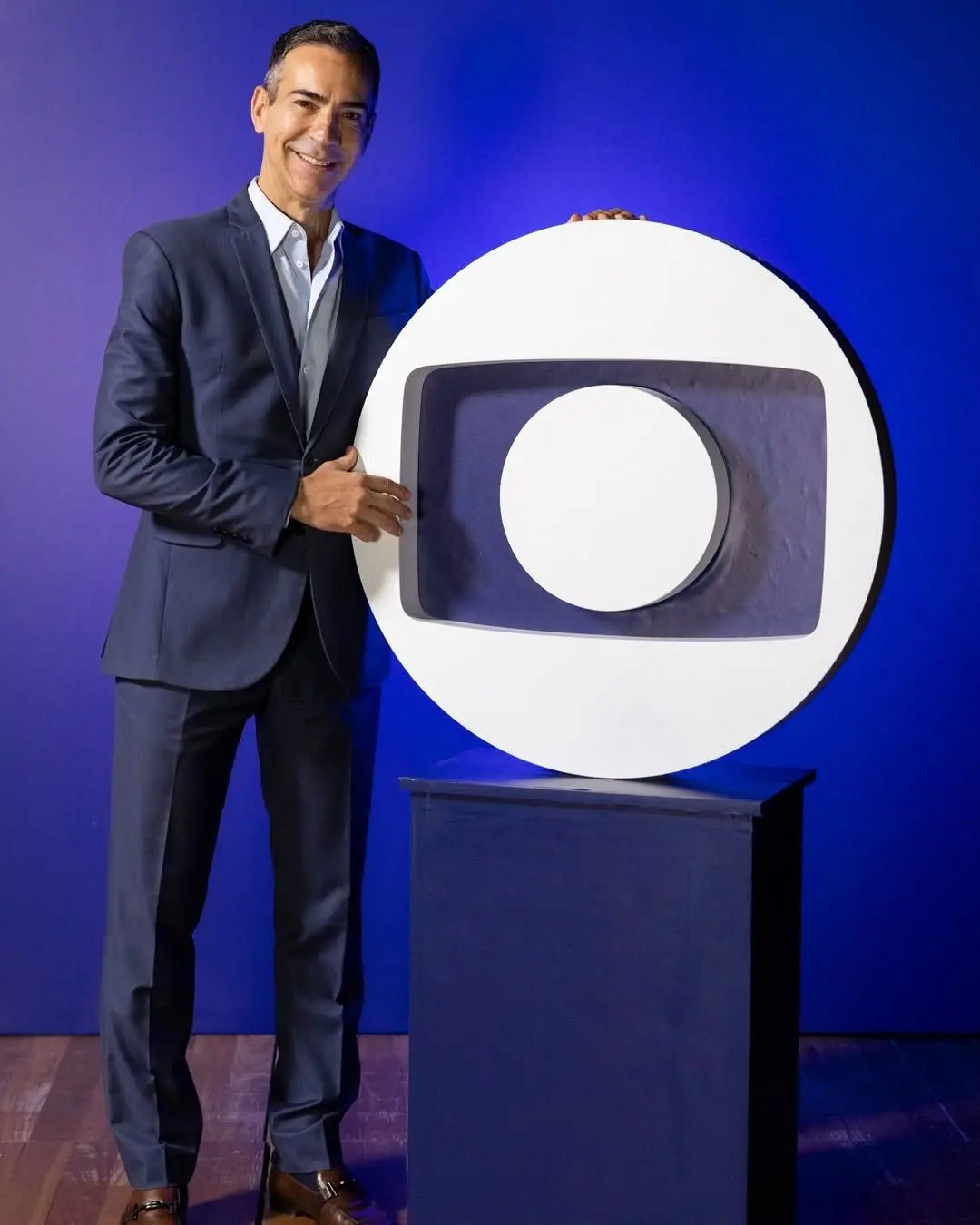 César Tralli sorrindo ao lado de símbolo da rede globo