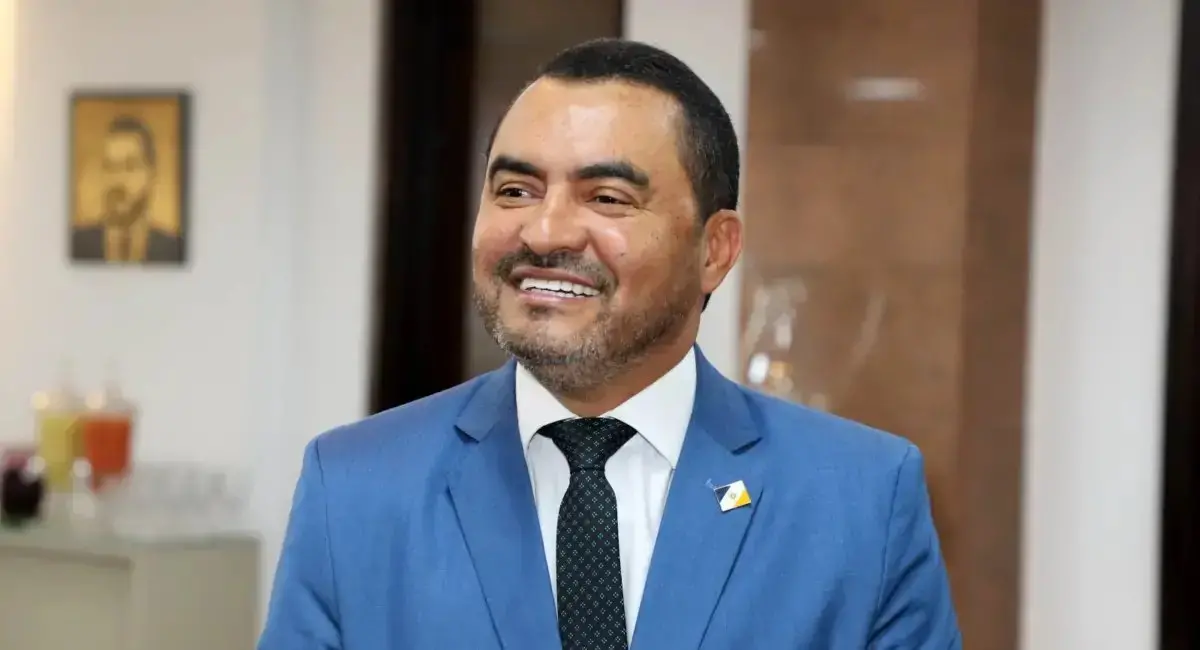 Homem sorridente vestido com terno azul e gravata, exalando confiança. Foto profissional em ambiente de escritório ou evento social.