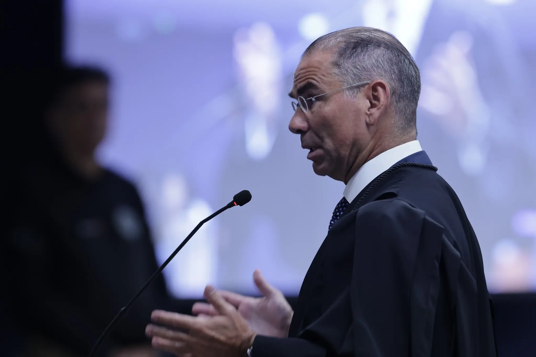 José Luís mendes de Oliveira Lima, diante do telão, faz a sustentação oral para os minitros