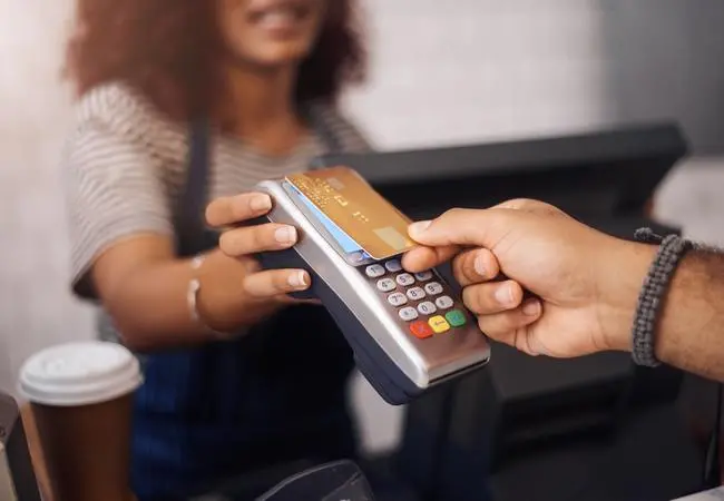 Máquina de cartão de crédito, café e mãos do cliente para compras b2c, transação de ponto de venda e finanças. De perto, pagamento por NFC e sem contato em cafeteria. Novas regras do cartão de crédito entram em vigor no Brasil: saiba o que muda
