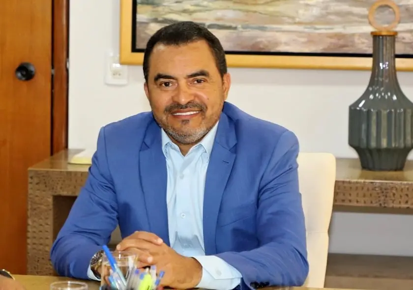 Homem de terno azul sentado em uma mesa de escritório com decoração moderna ao fundo