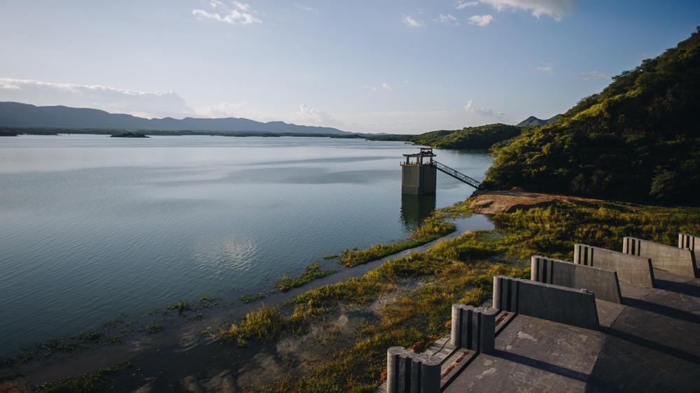 Vista panorâmica do açude Orós, cercado por vegetação e montanhas ao fundo, com estrutura de captação de água no centro