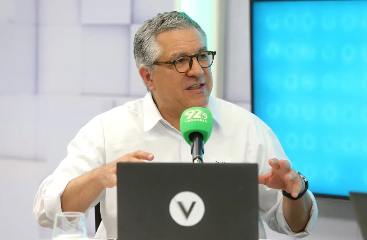 Ministro Alexandre Padilha, homem de cabelos grisalhos e de óculos, fala em frente a um microfone verde da rádio 92.5 Verdinha, durante entrevista em estúdio.